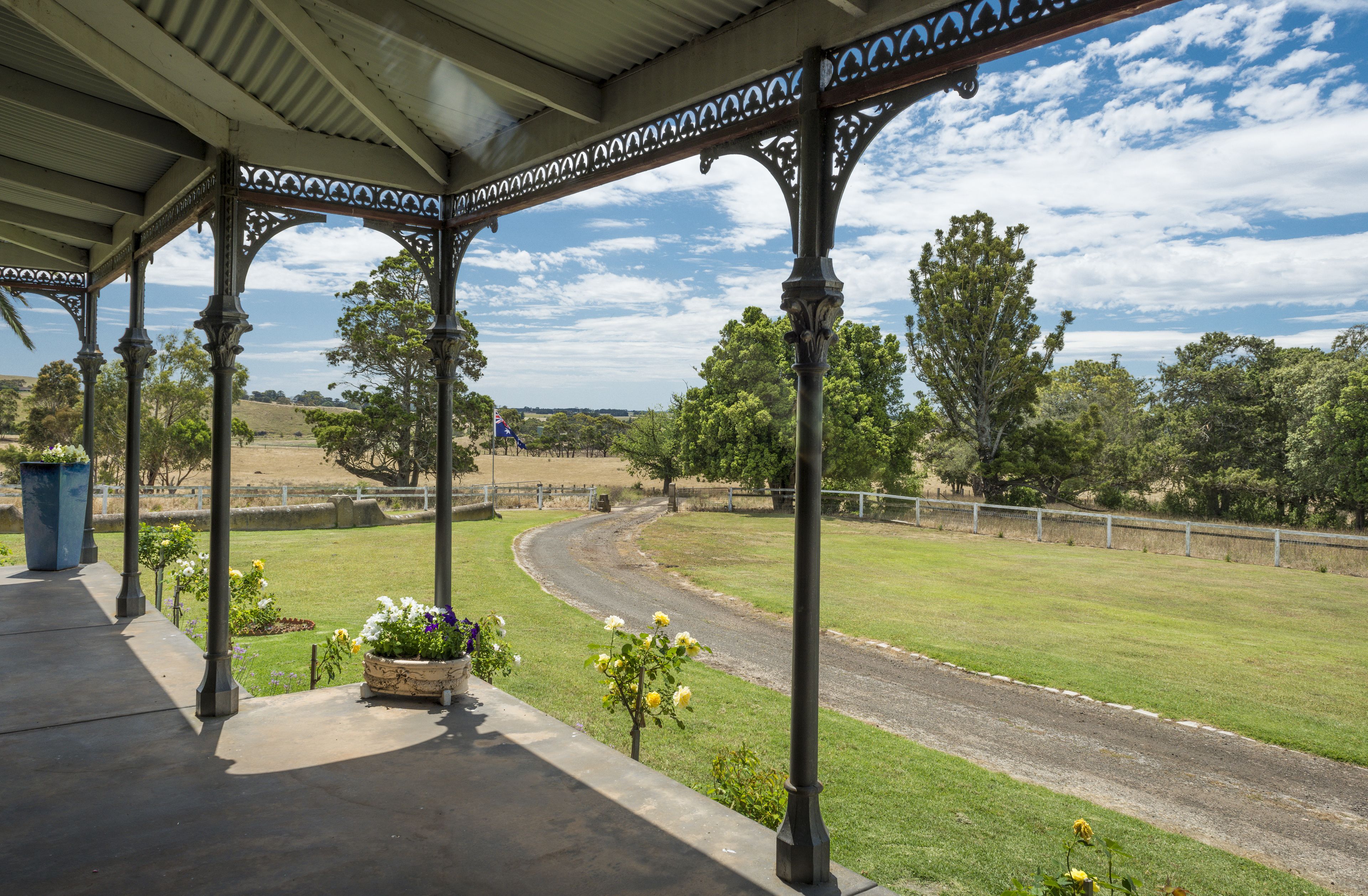 A covered outdoor area with a curved pathway, surrounded by greenery and a fence.