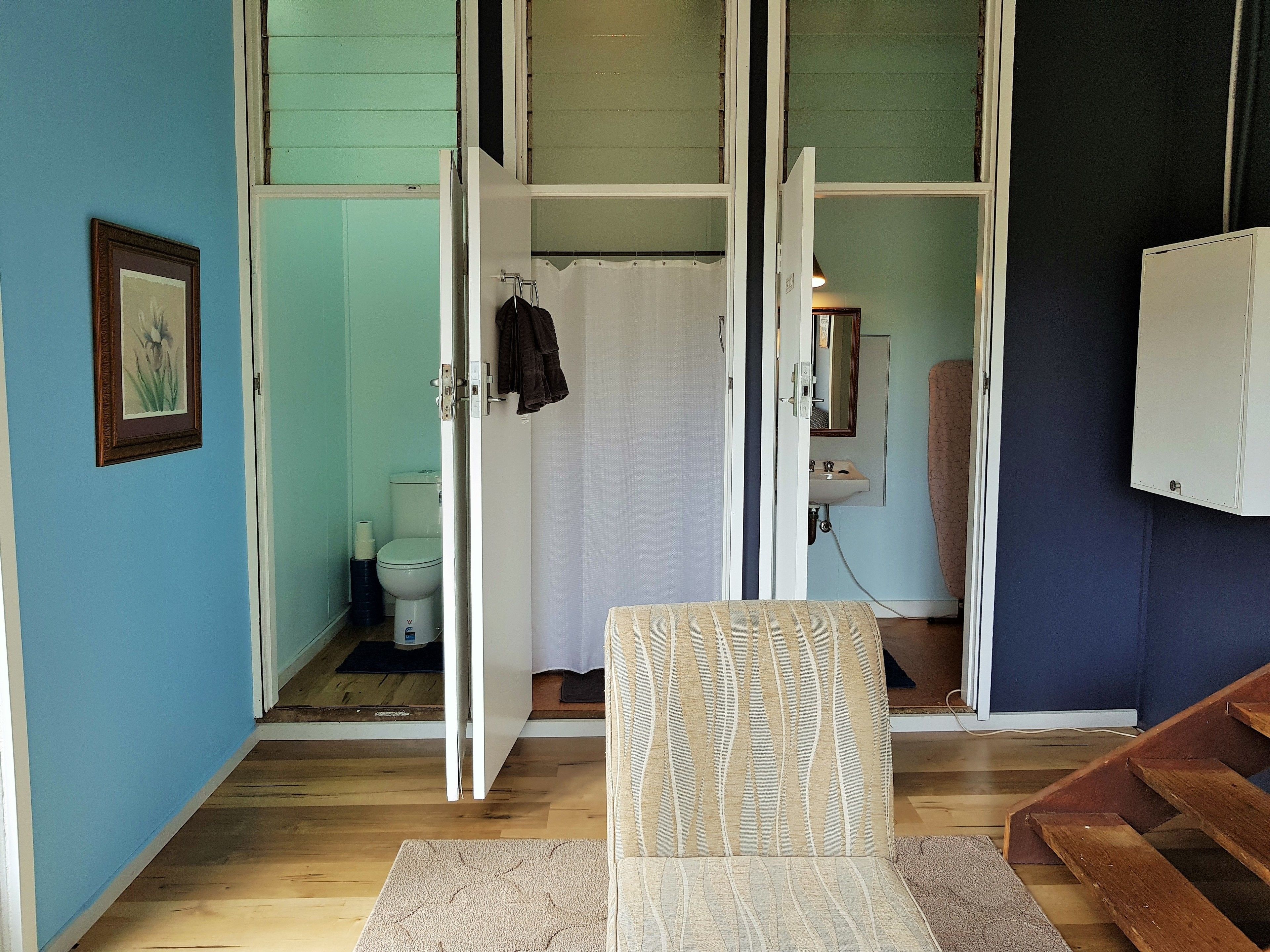 A bathroom with a toilet, sink, and shower curtain. There is a chair and a wooden bench.