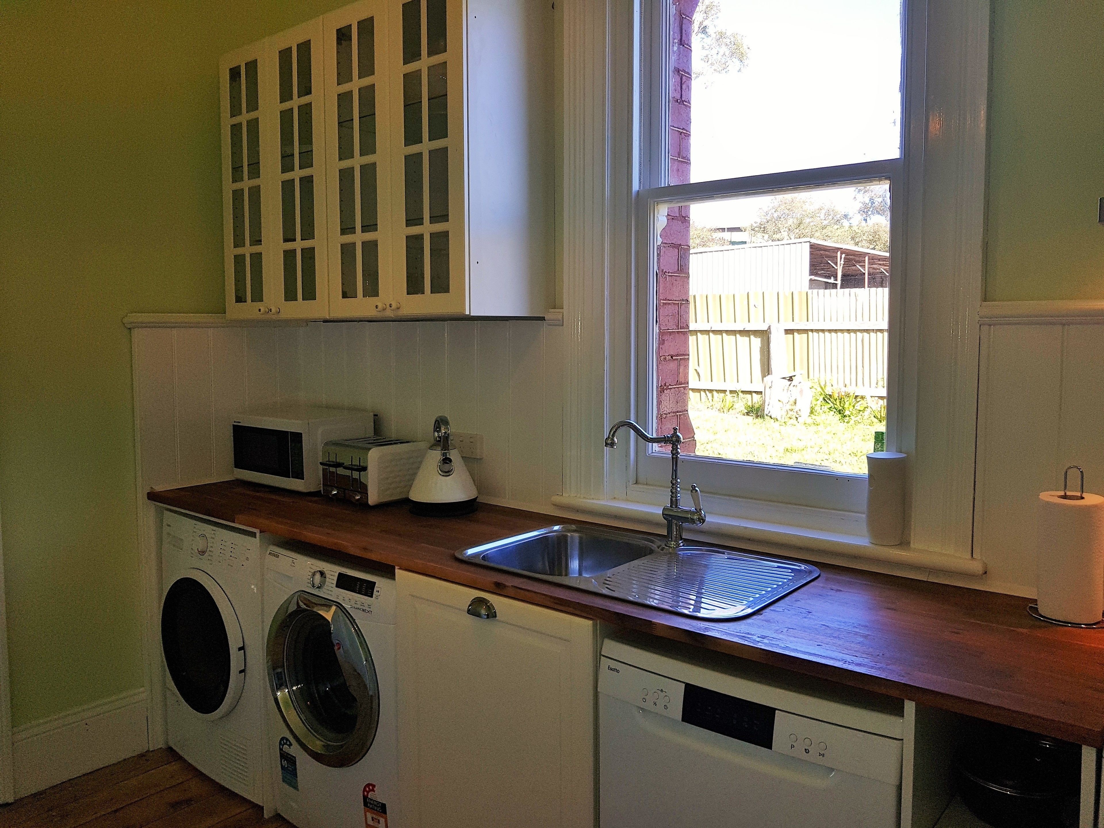 Een compacte keuken met een wasmachine, een broodrooster en een gootsteen onder een raam.