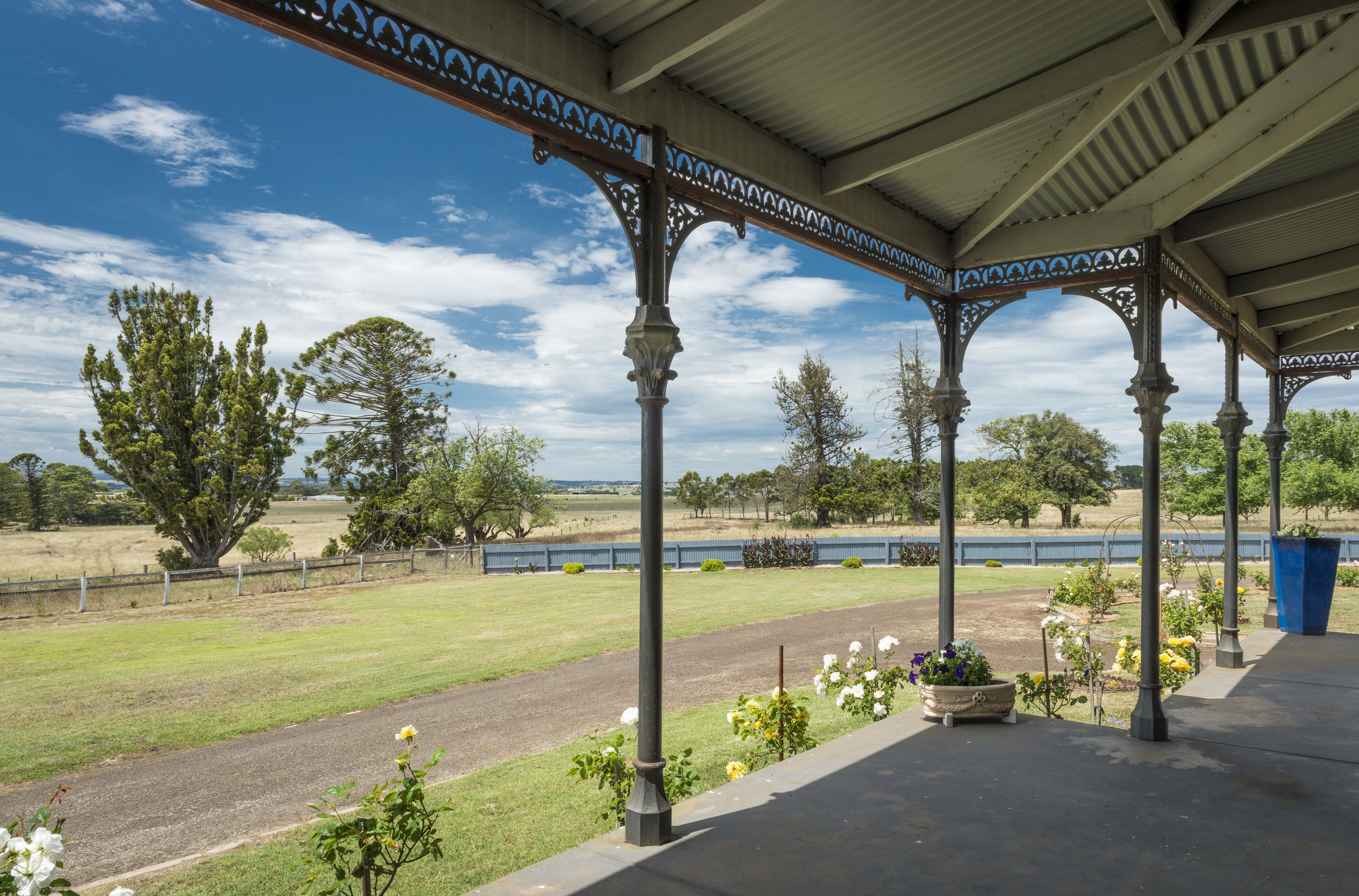 A covered pavilion with ornate columns and a view of a grassy field and trees.