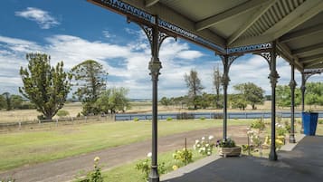A covered pavilion with ornate columns and a view of a grassy field and trees.