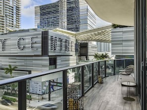 Un edificio moderno con fachada de vidrio, mesas al aire libre y vista de la calle.