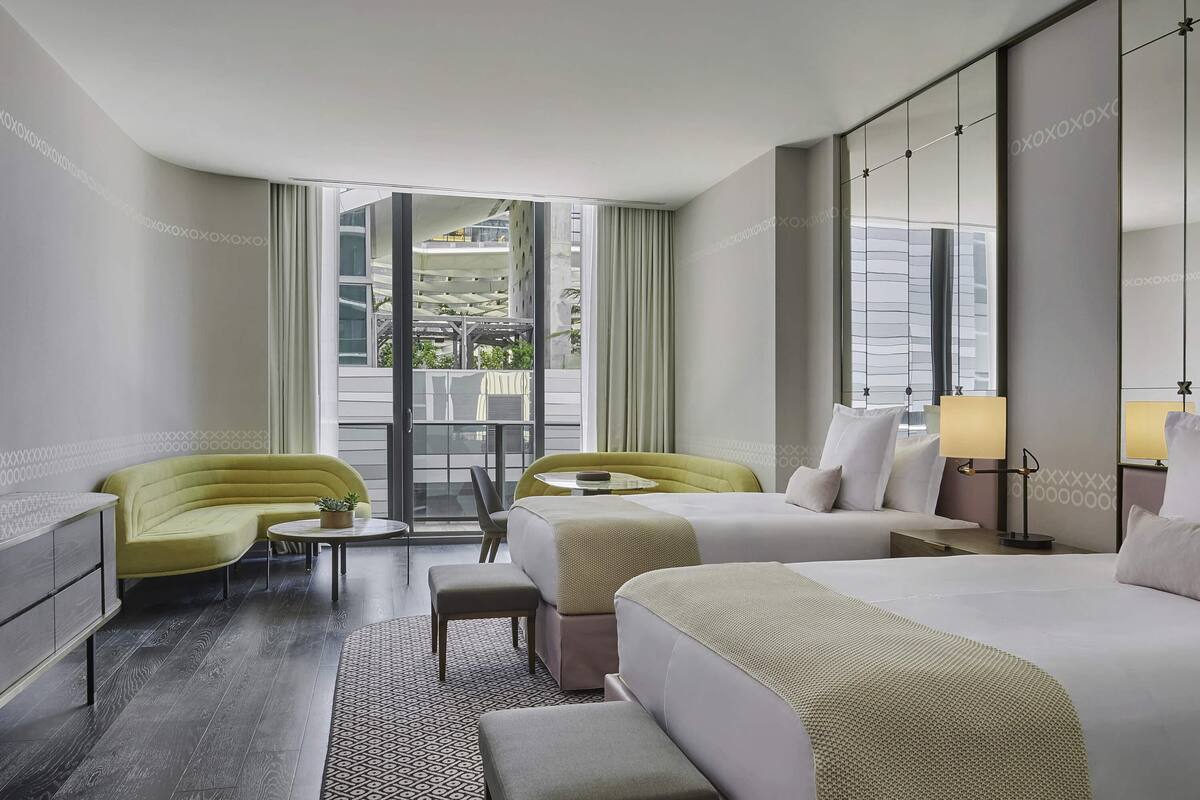 Ein modernes Hotelzimmer mit zwei Betten, einer Couch, einem kleinen Tisch und einem Balkon mit Blick auf eine Parkgarage.