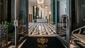 L’entrée d’un hôtel, avec son sol à carreaux, un comptoir d’accueil et un grand lustre.