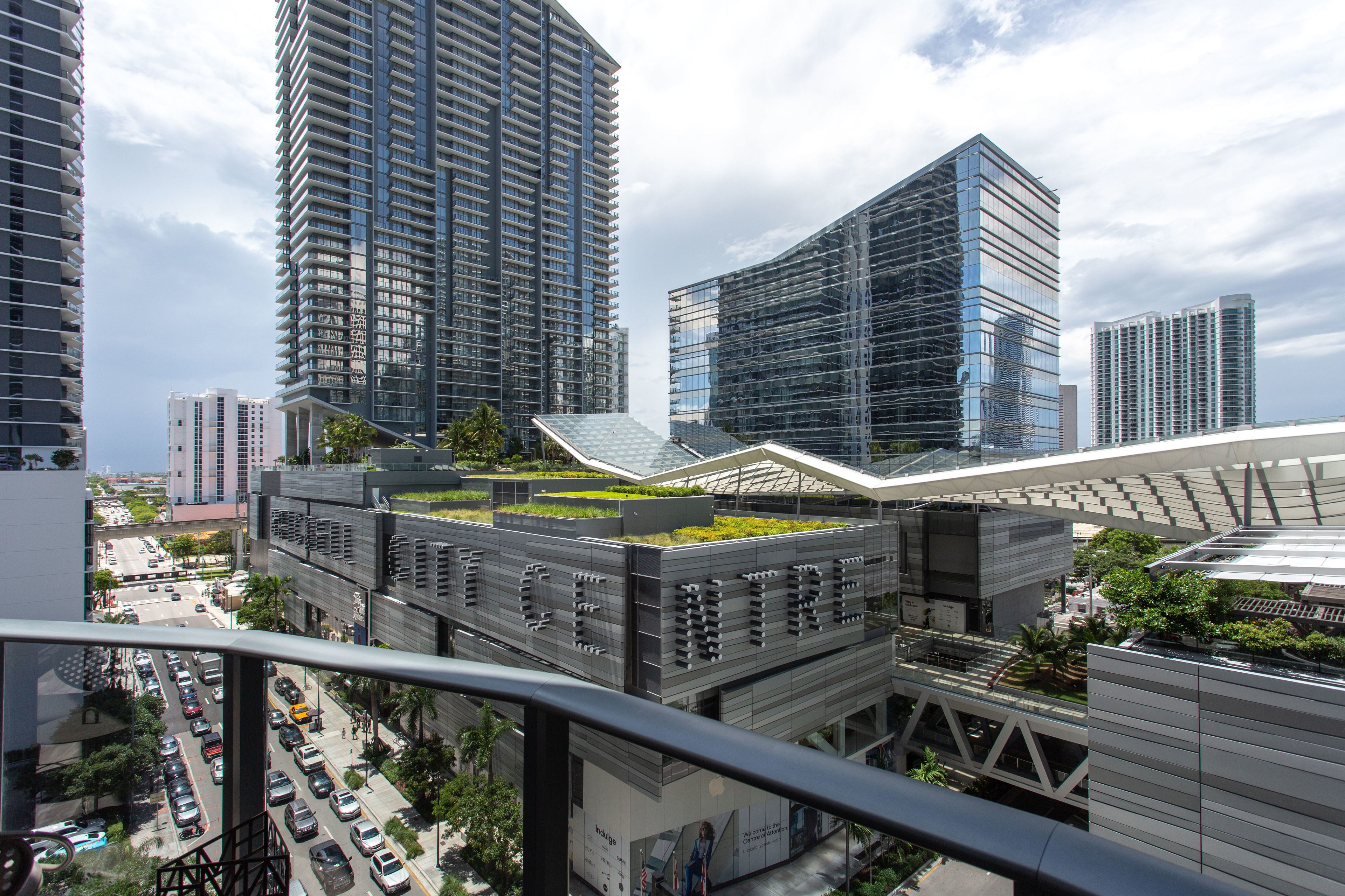 A modern building with a rooftop garden, surrounded by high-rise buildings.