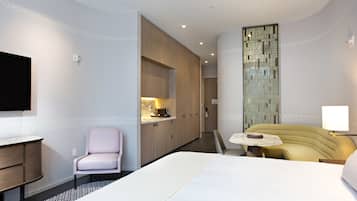 Una habitación de hotel moderna con una cama grande, un escritorio pequeño, una silla, un sofá y un televisor montado en la pared.
