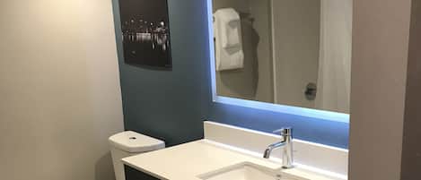 Casa de banho moderna com sanita branca, lavatório com espelho e um porta-toalhas.