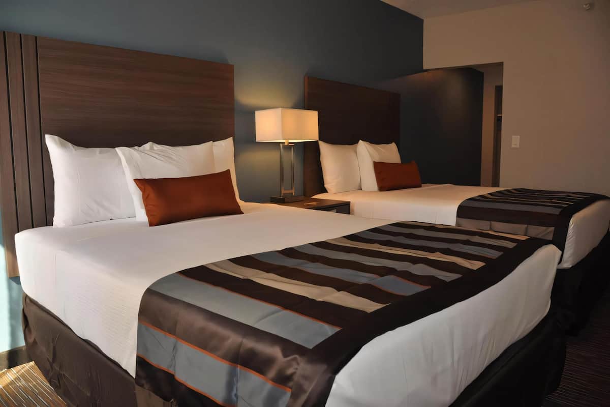 Een hotelkamer met twee bedden, een nachtkastje met een lamp en uitzicht op de gang.