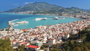 A coastal town with a marina, buildings with red roofs, and a mountainous backdrop. - Home Away Junior Suite (Zakynthos)