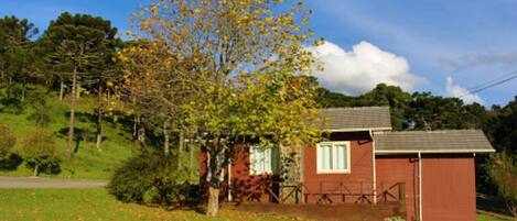 A small red building with a white window and a door, surrounded by a grassy area with fallen leaves.