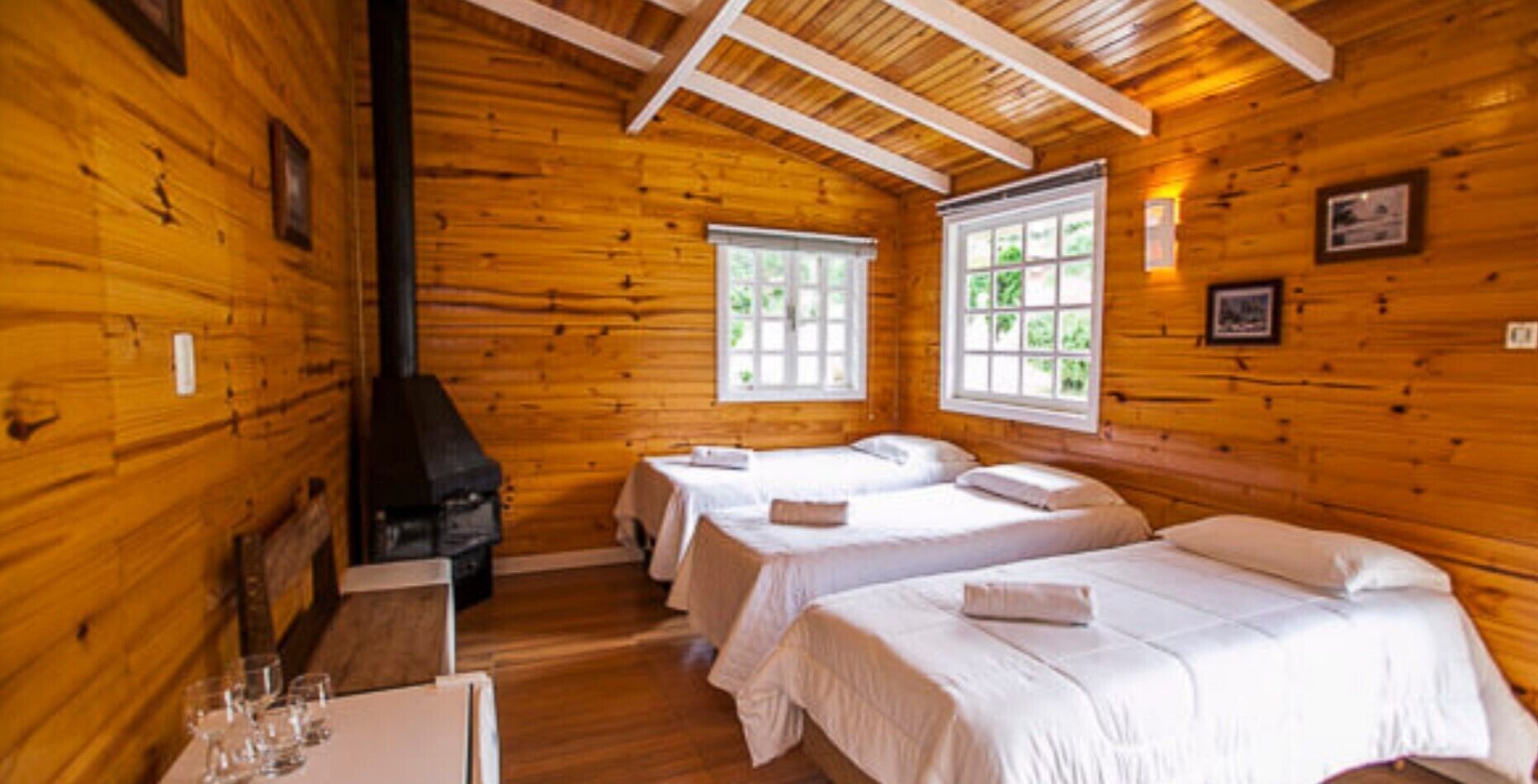Una cabaña con paredes de madera, dos camas, una chimenea y dos ventanas.