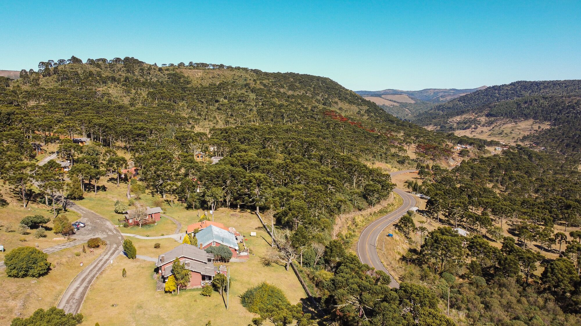 An aerial view of a rural area with scattered houses, winding roads, and dense vegetation on rolling hills.