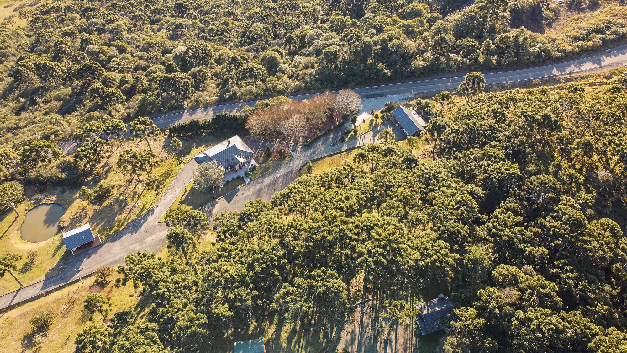 Vue aérienne d’une propriété comprenant une maison principale, un bâtiment plus petit et un étang.
