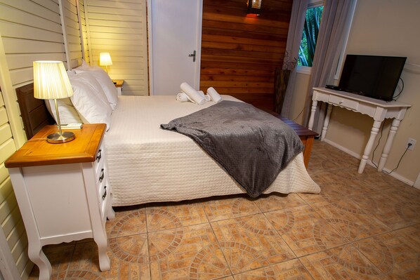 Un lit bien fait, recouvert d’une couverture grise, avec une lampe de chevet et une table de nuit en bois.