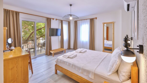 Un dormitorio con cama, escritorio, silla, televisor y balcón con mesa y sillas.