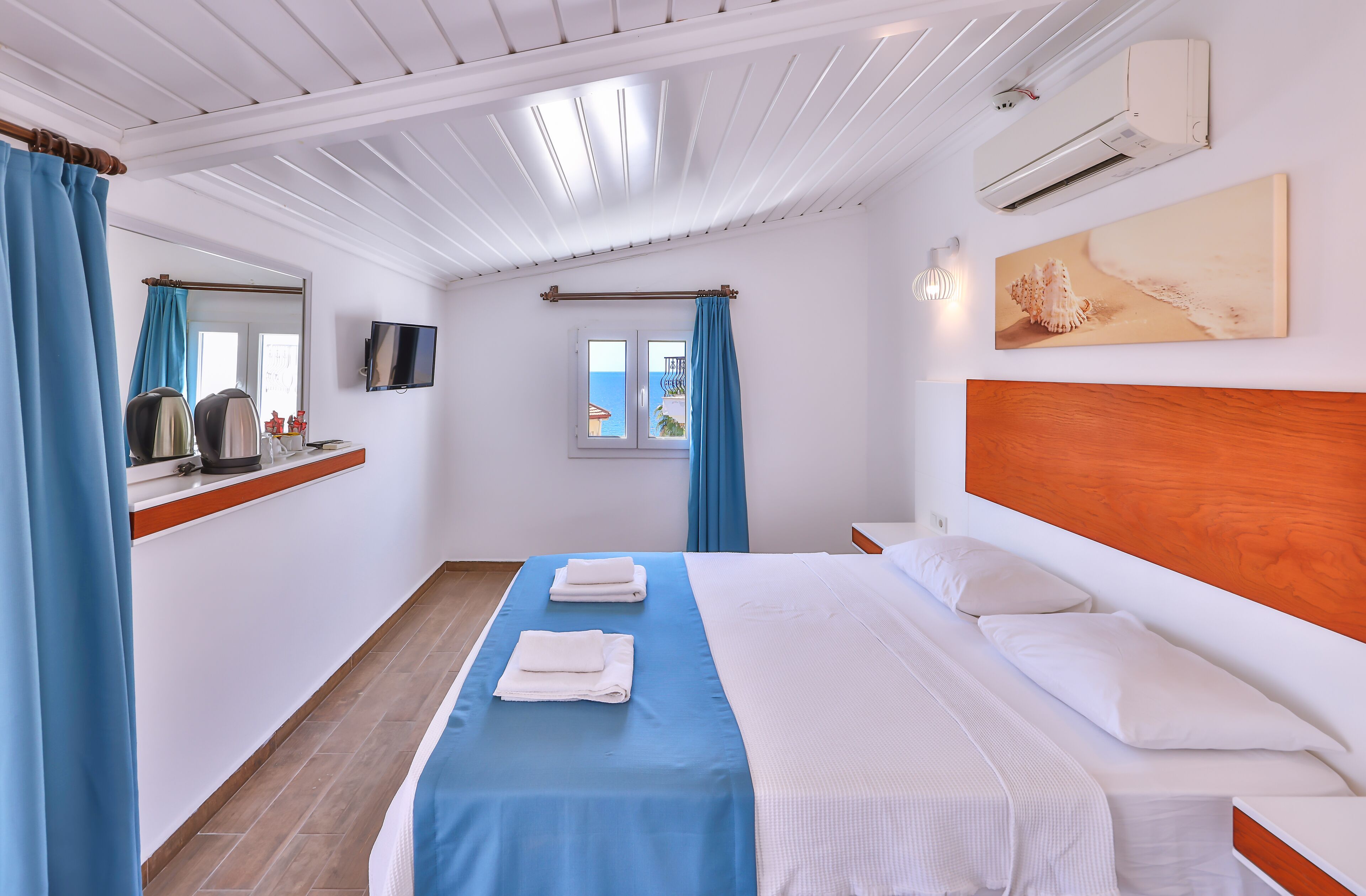 Una habitación de hotel con cama, televisión, ventana con cortinas, un cuadro y aire acondicionado.