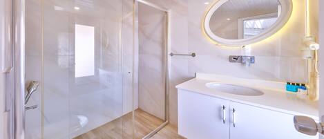 Une salle de bain moderne avec une douche à parois de verre, un lavabo blanc et un miroir rond doté d’un cadre éclairé.