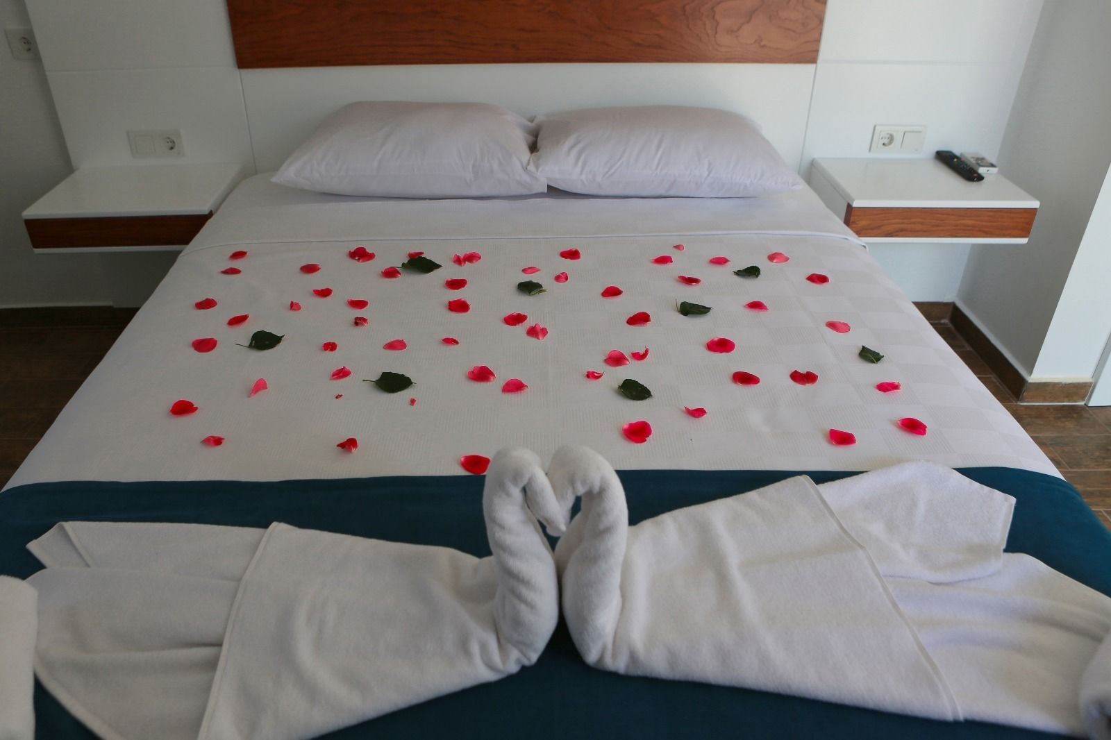 Een net opgemaakt bed met rozenblaadjes en handdoeken.