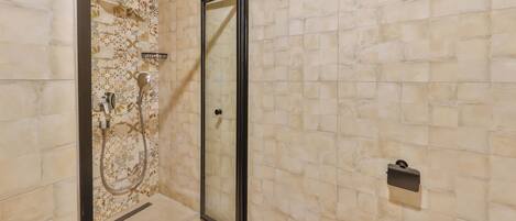 A shower with a glass door, a towel rack, and a wall with patterned tiles.