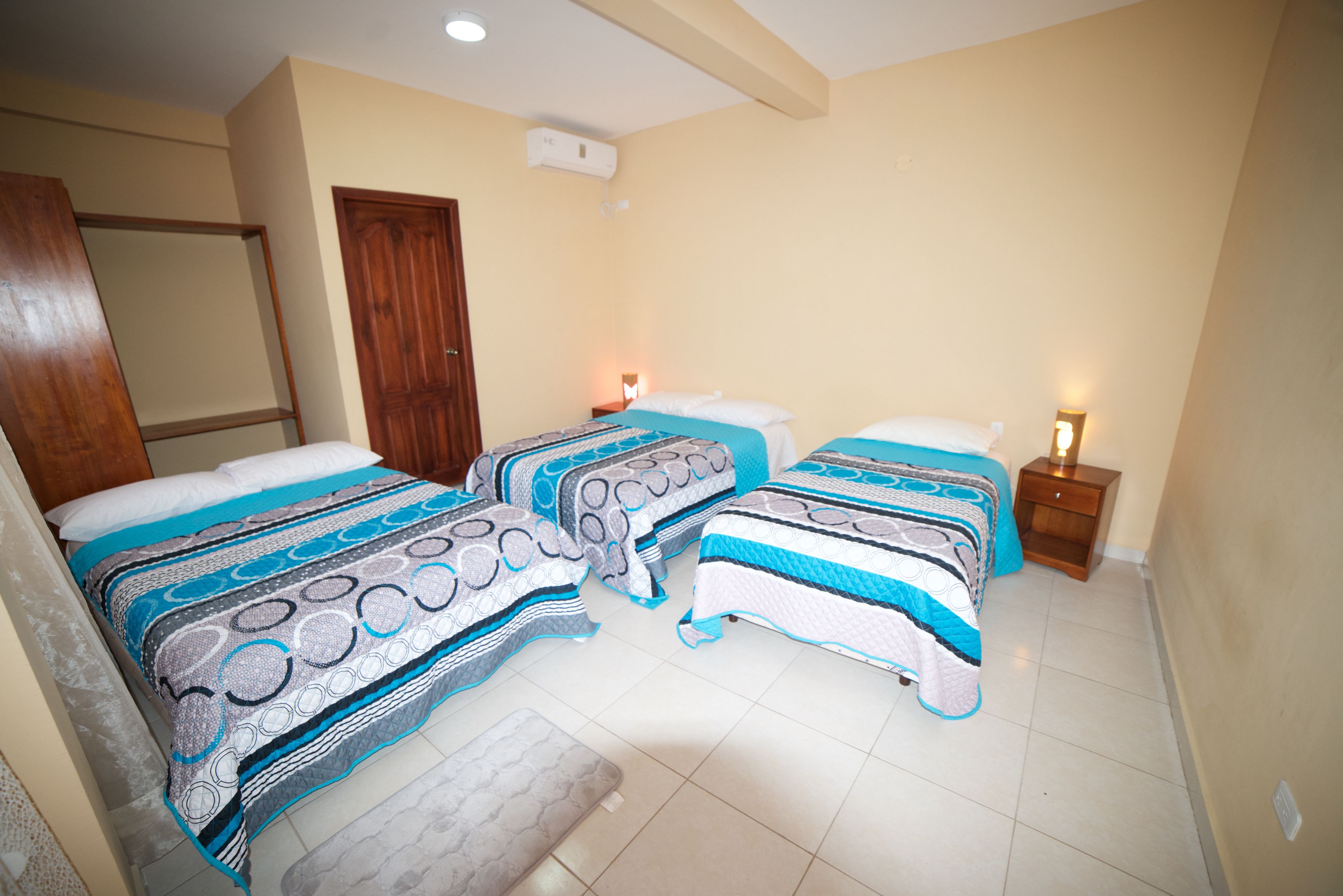 A bedroom with two beds, each with patterned bedding, a wooden door, and a nightstand with a lamp.