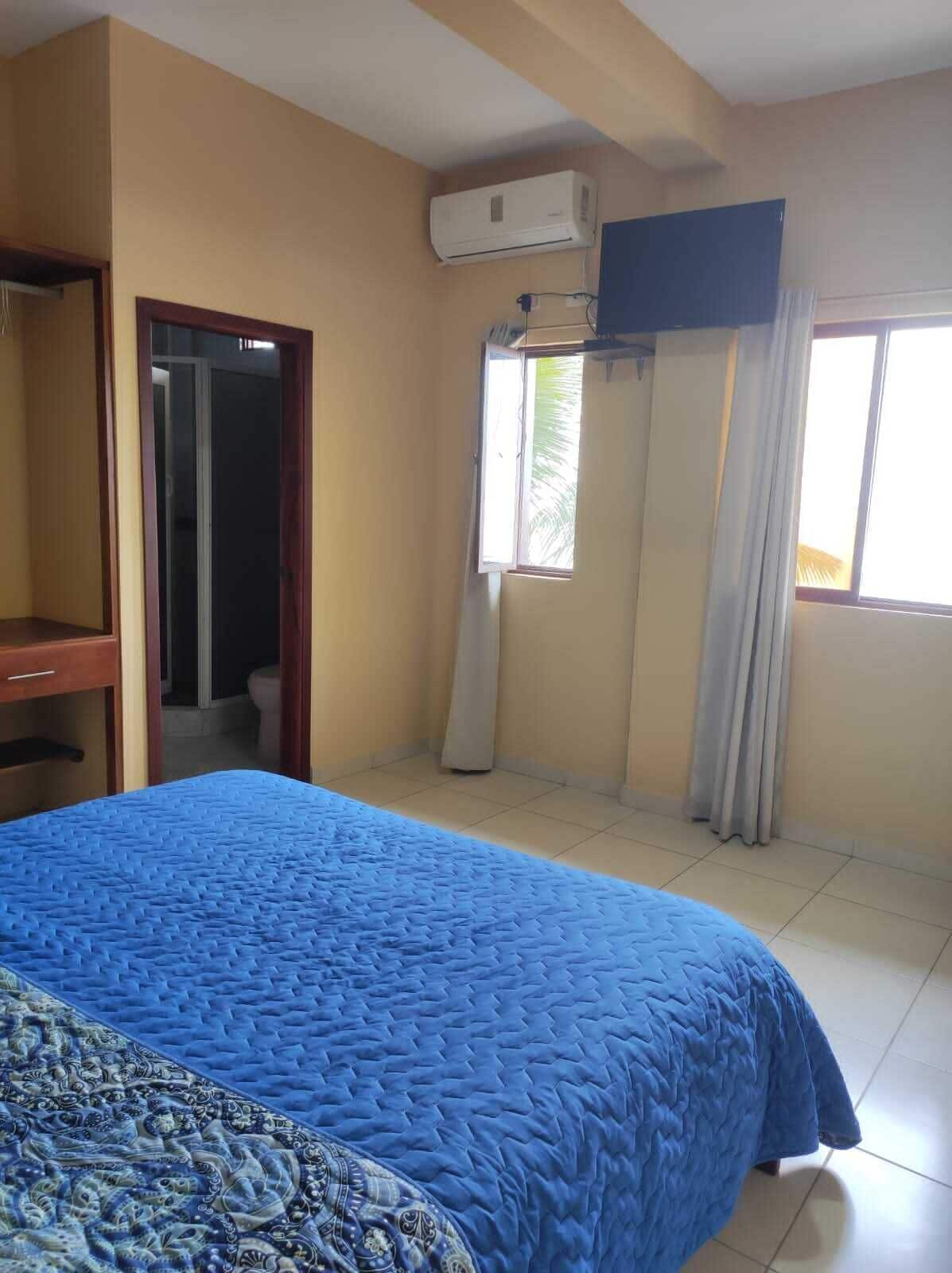 Ein Schlafzimmer mit Bett, Kleiderschrank, einem Fenster mit Vorhängen und einer Klimaanlage.