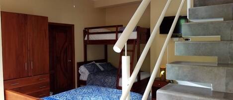 A bedroom with a bunk bed, a wooden wardrobe, a ceiling fan, and a staircase.