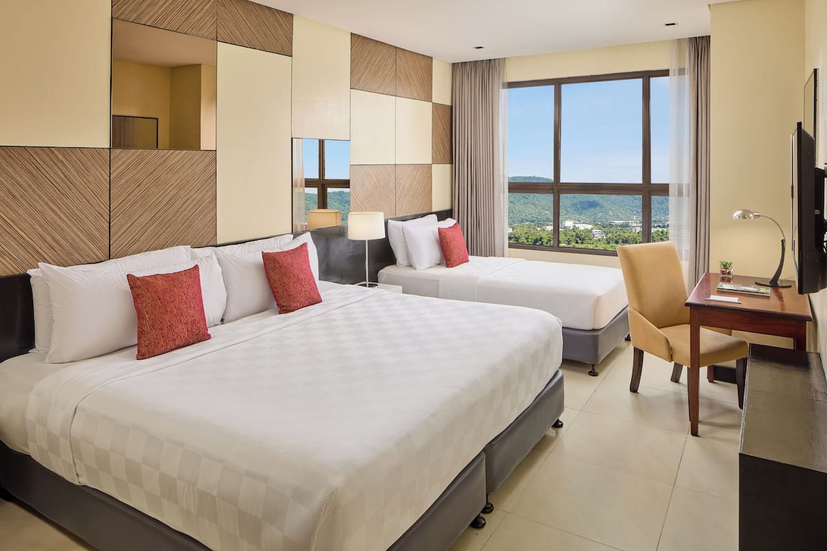A hotel room with two beds, a desk, a chair, and a large window offering a city view.