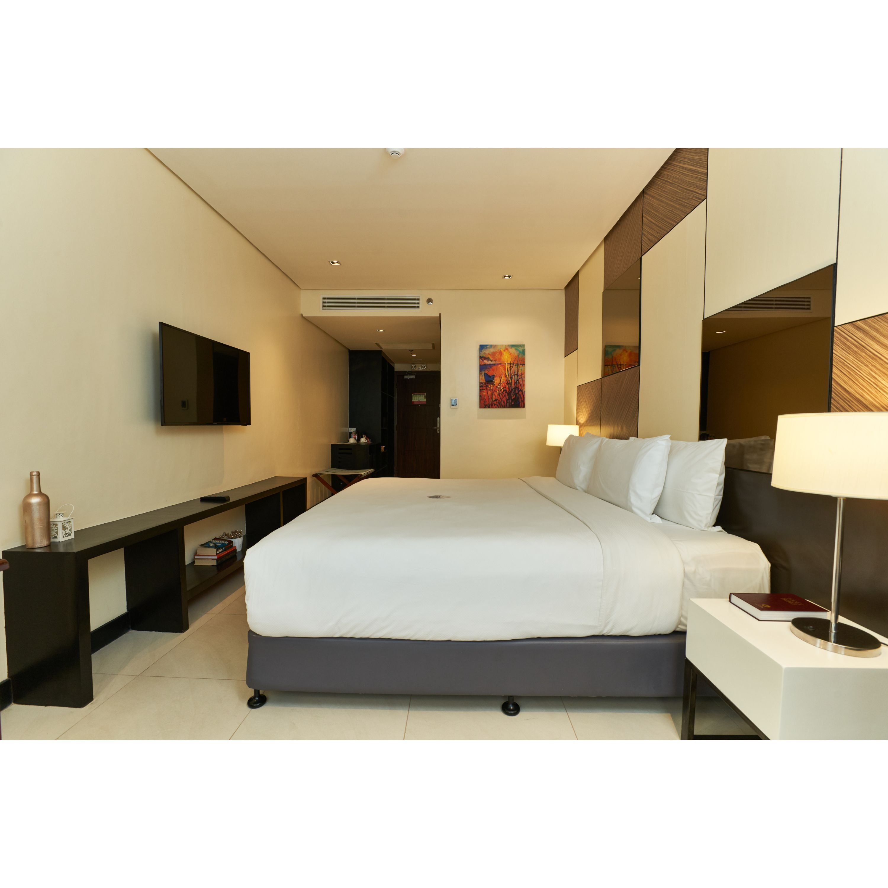 Een moderne hotelkamer met een groot bed, nachtkastjes, een flatscreen-tv en een schilderij aan de muur.