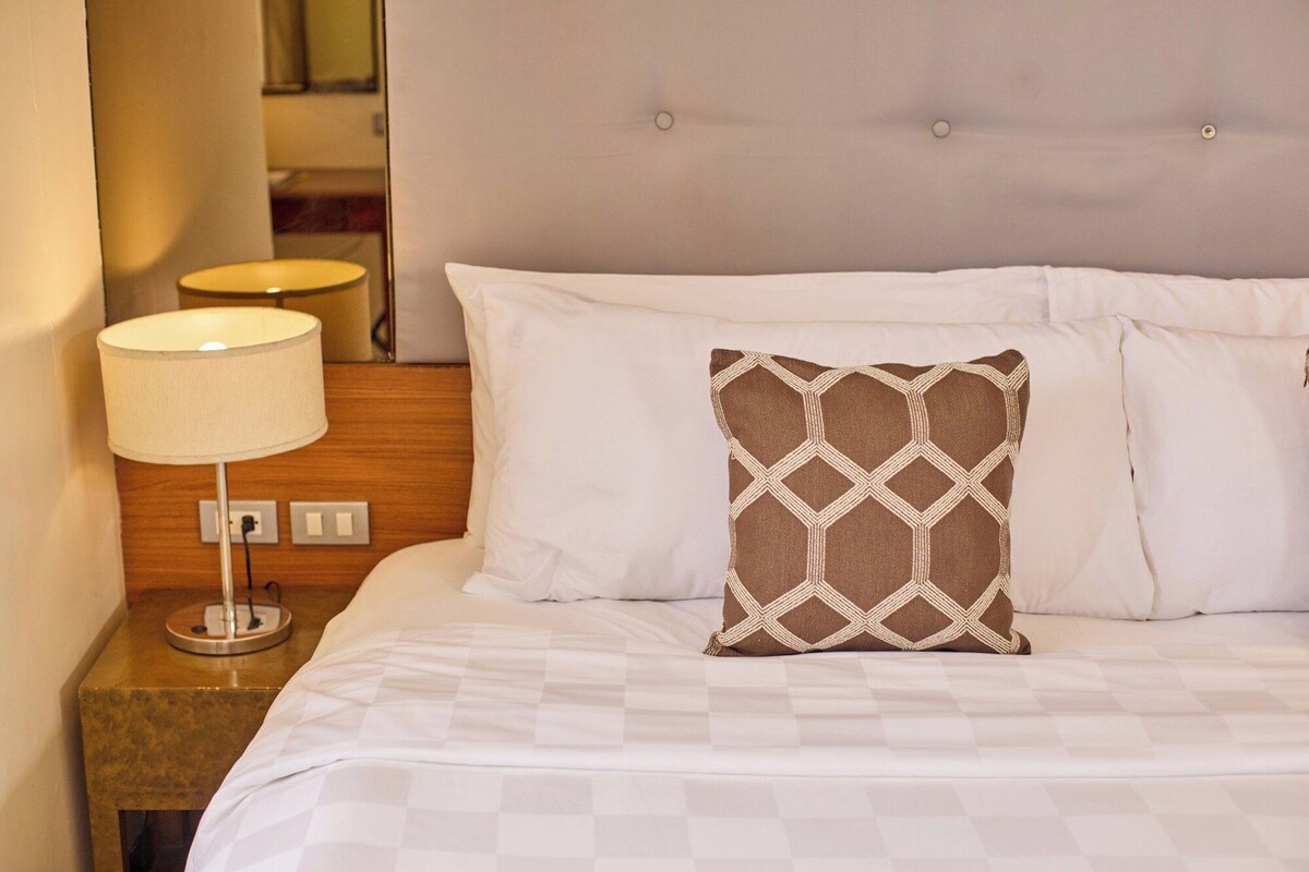 A hotel room with a bed, a nightstand, a lamp, and a mirror.