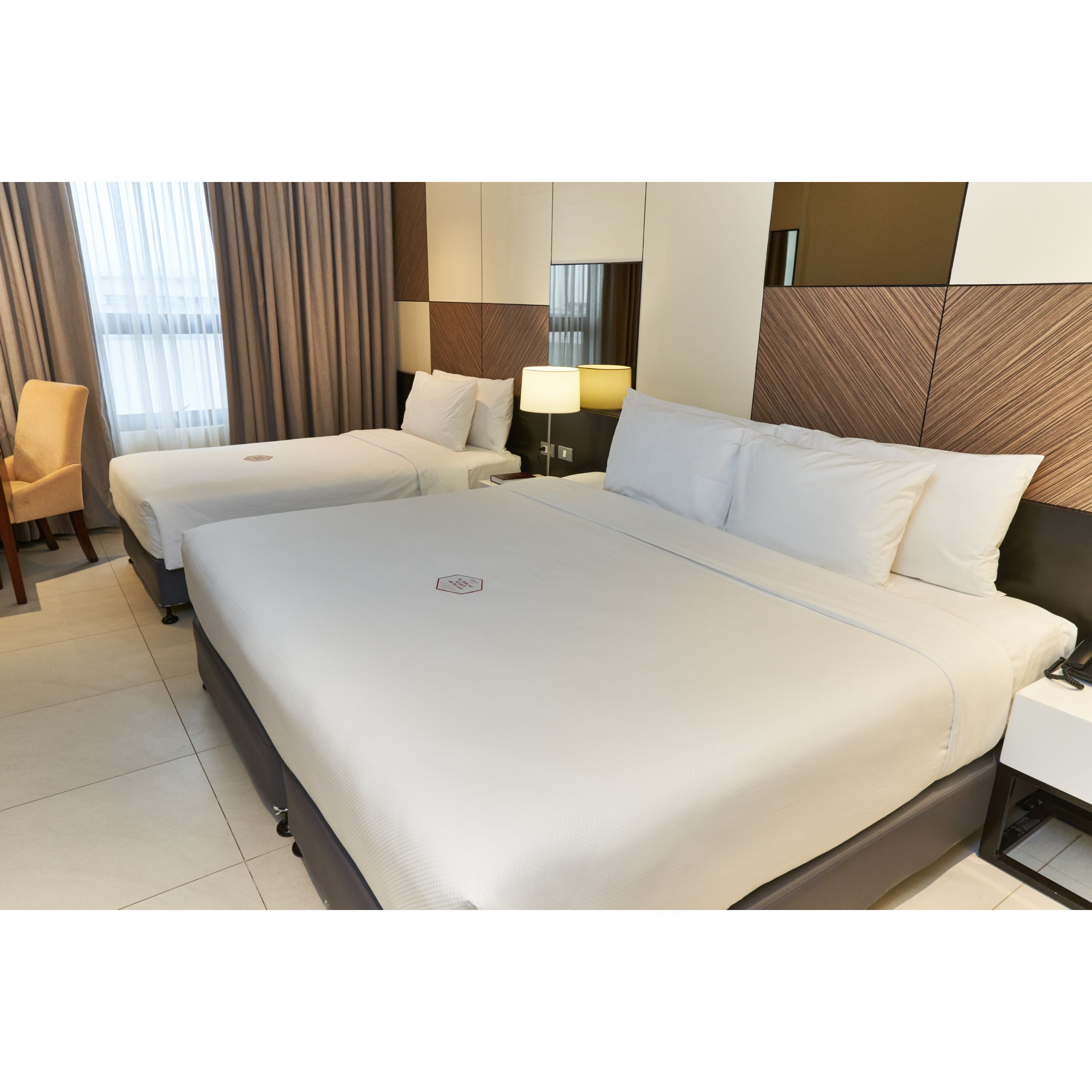 A hotel room with two beds, a chair, a nightstand, and a lamp.