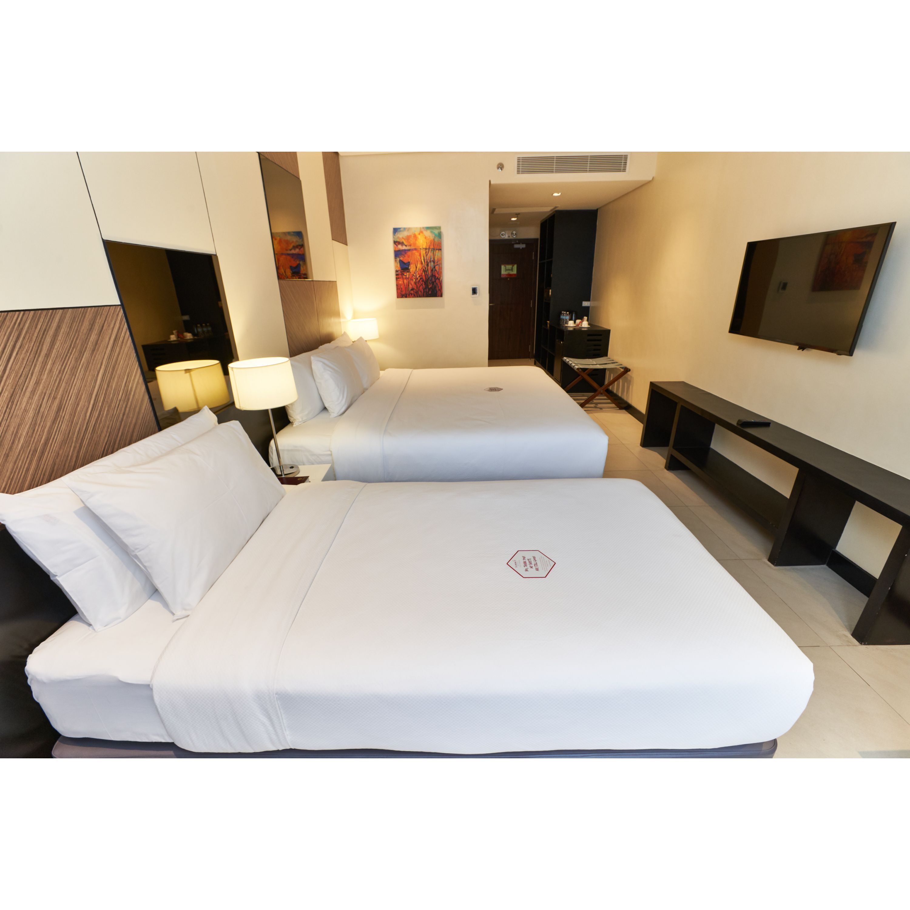 Een hotelkamer met twee bedden, een bureau, een televisie en kunst aan de wanden.