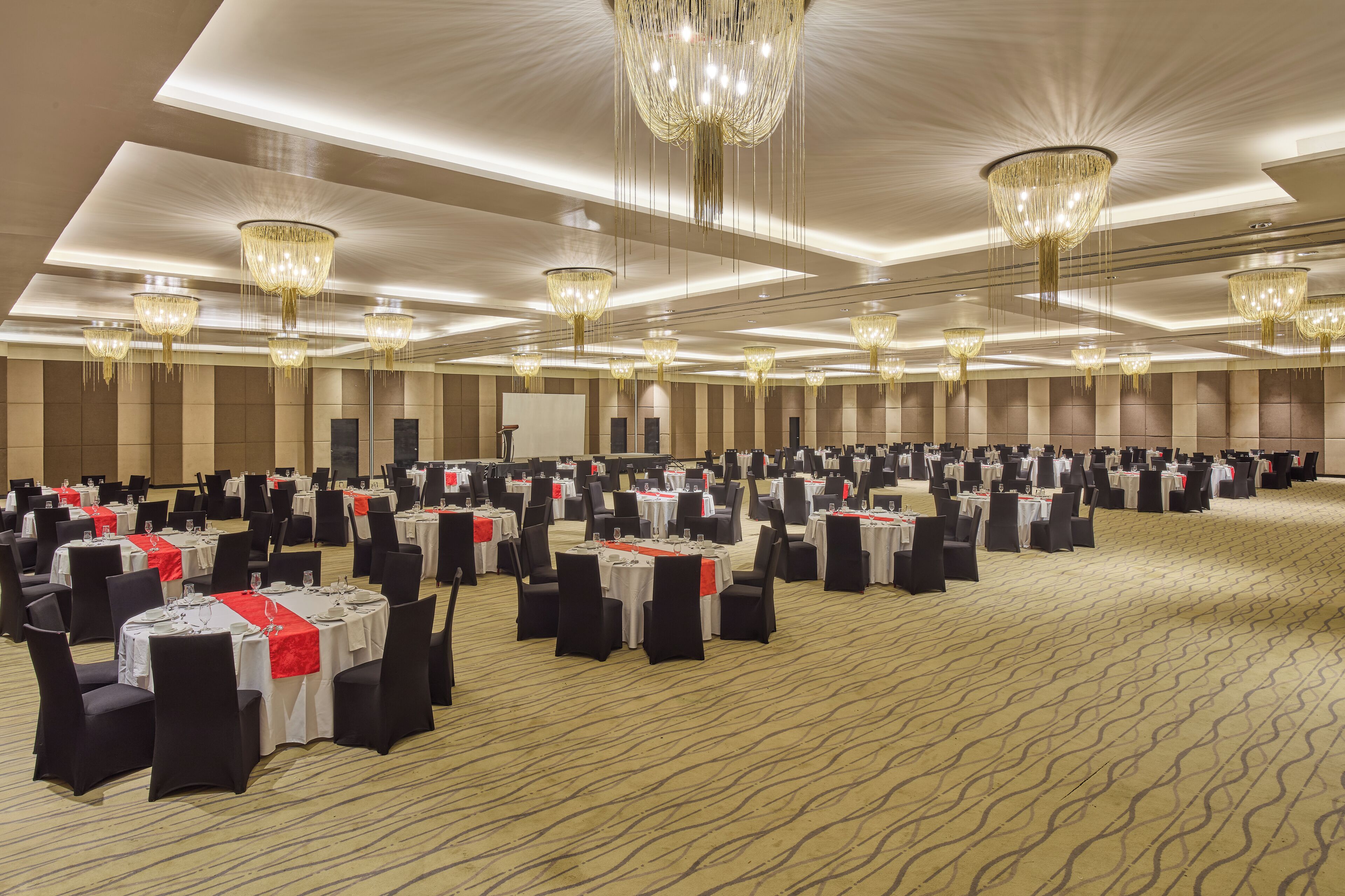 A large banquet hall with multiple tables and chairs, chandeliers, and a carpeted floor.