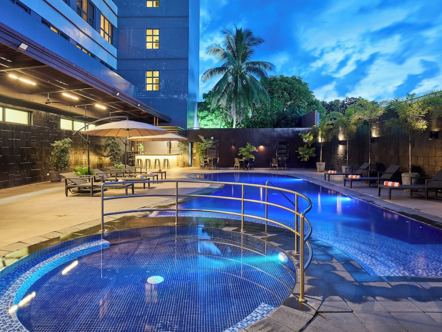 A swimming pool with a tiled deck, lounge chairs, and a palm tree in the background.
