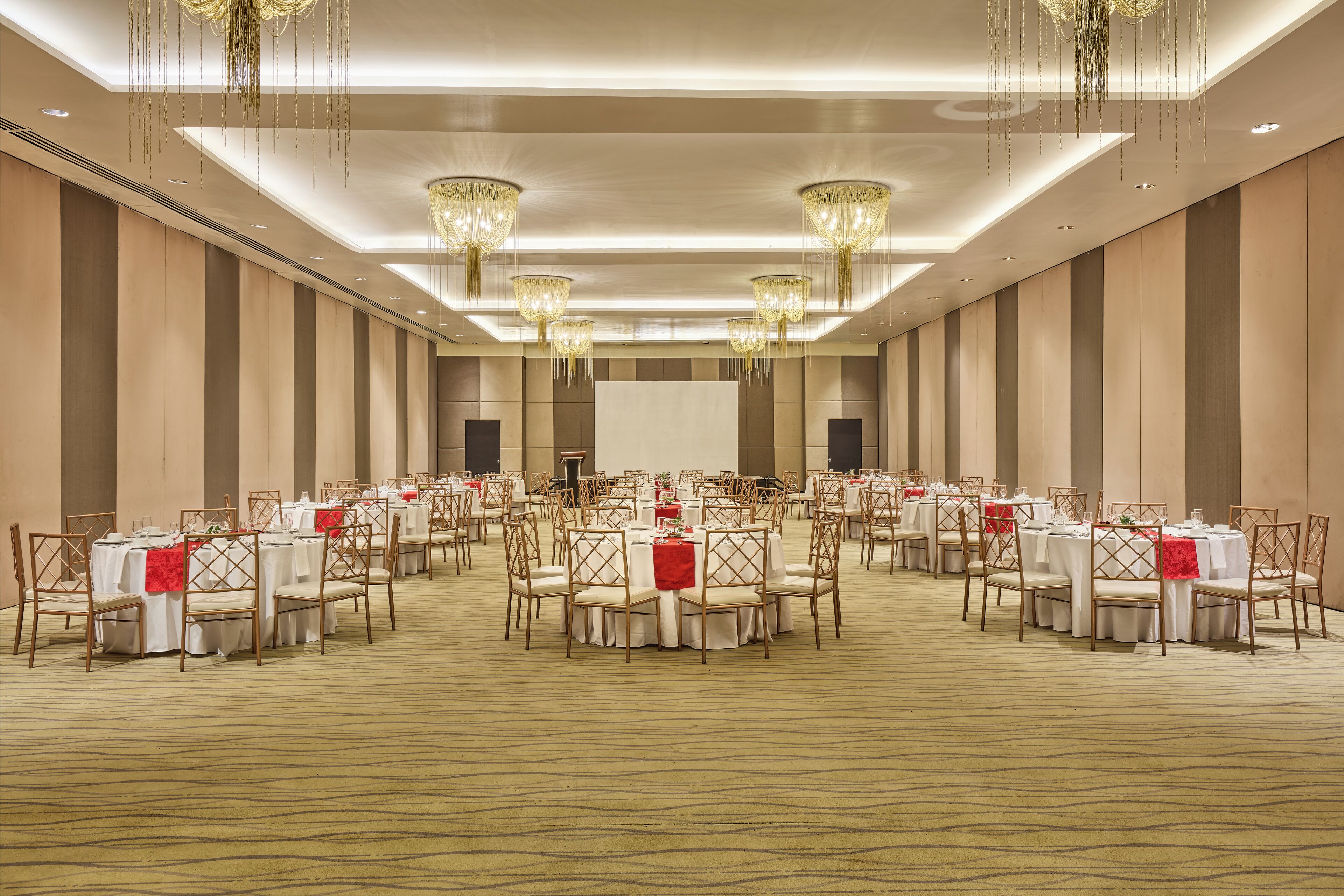 Une grande salle de banquet avec des tables rondes et des chaises, des lustres et une scène.