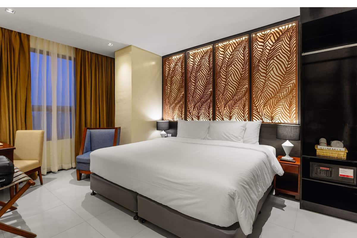 A modern hotel room with a large bed, a desk, a chair, and a decorative wall panel.