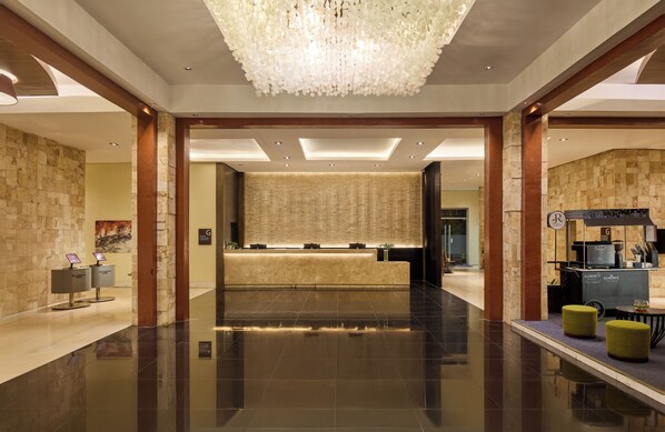 Um hall amplo com piso lustroso, balcão de recepção, lustre e estação de café.