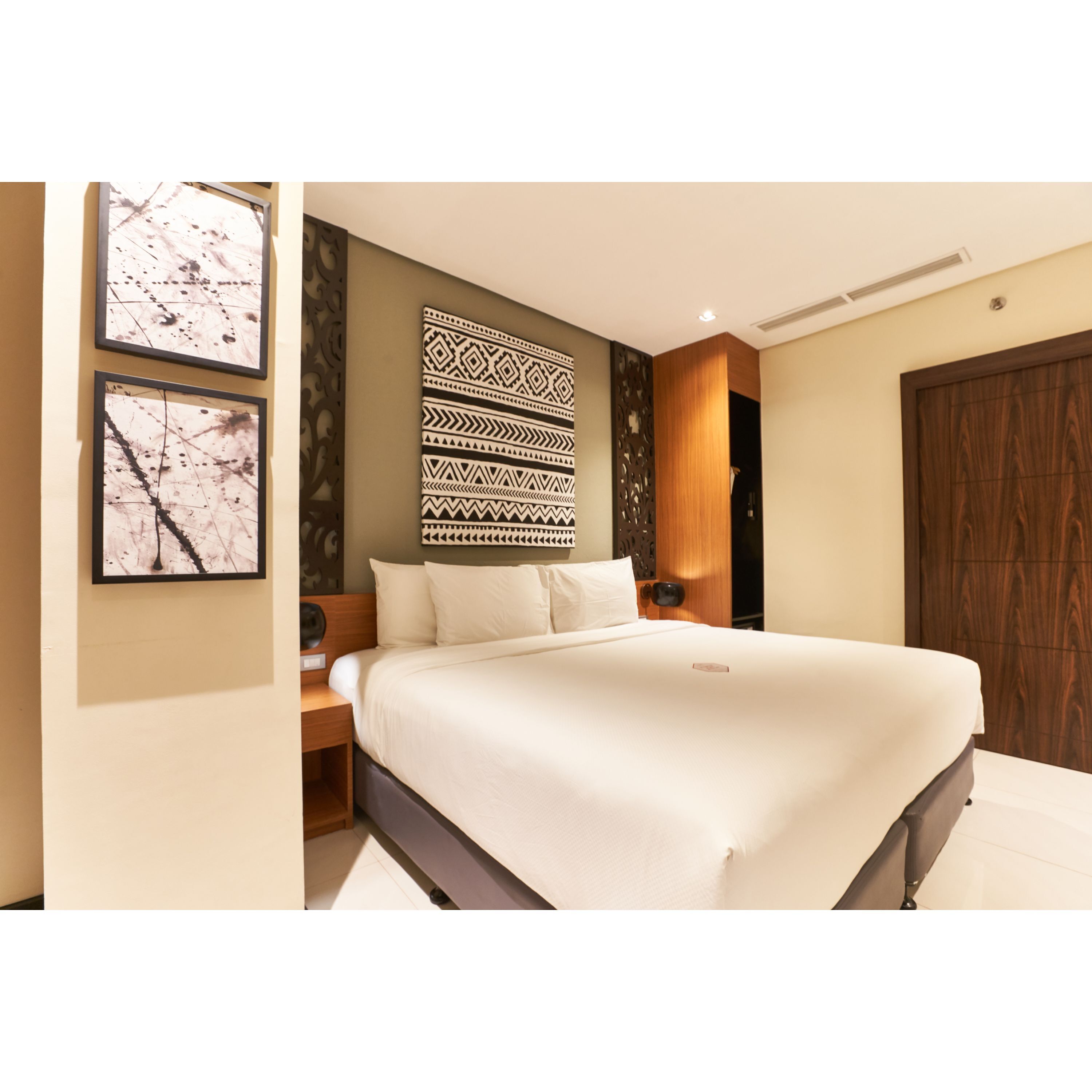 A modern hotel room with a large bed, a decorative wall panel, and a wooden wardrobe.
