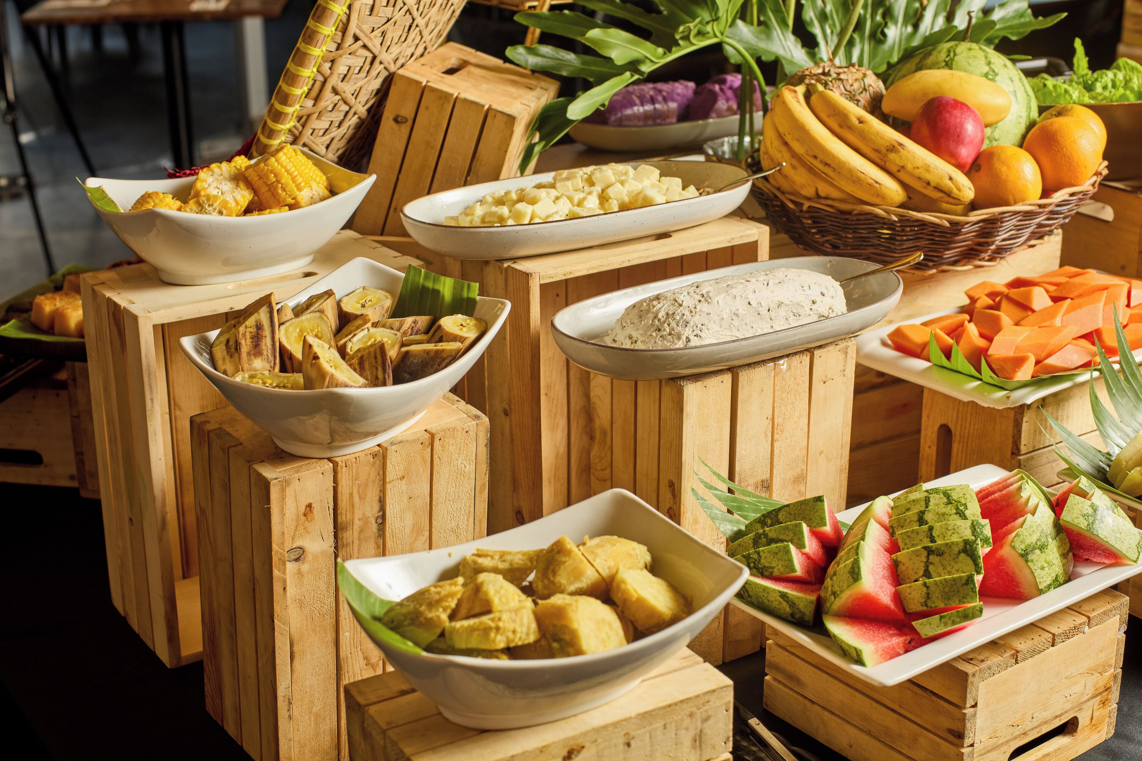 A variety of food items displayed on wooden crates, including corn, bananas, and watermelon.