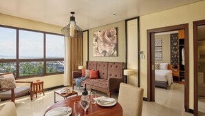 A hotel room with a large window, a sofa, a dining table set for two, and a bed with a nightstand. - Summit Hotel Tacloban (Tacloban)