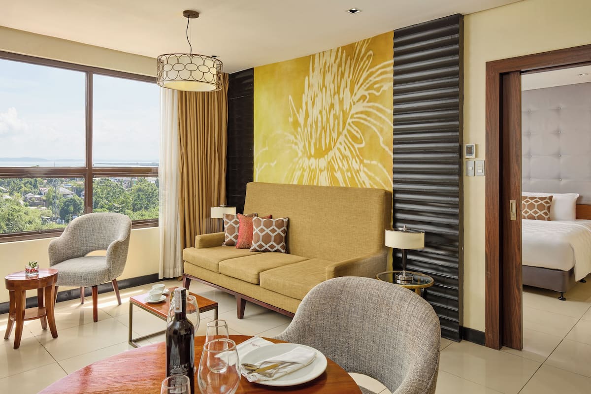 A hotel room with a sofa, armchairs, a dining table, and a bed.