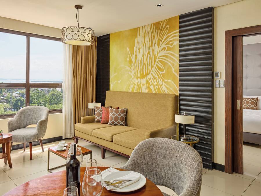 Ein Hotelzimmer mit einer Couch, Sesseln, einem Esstisch und einem Bett.