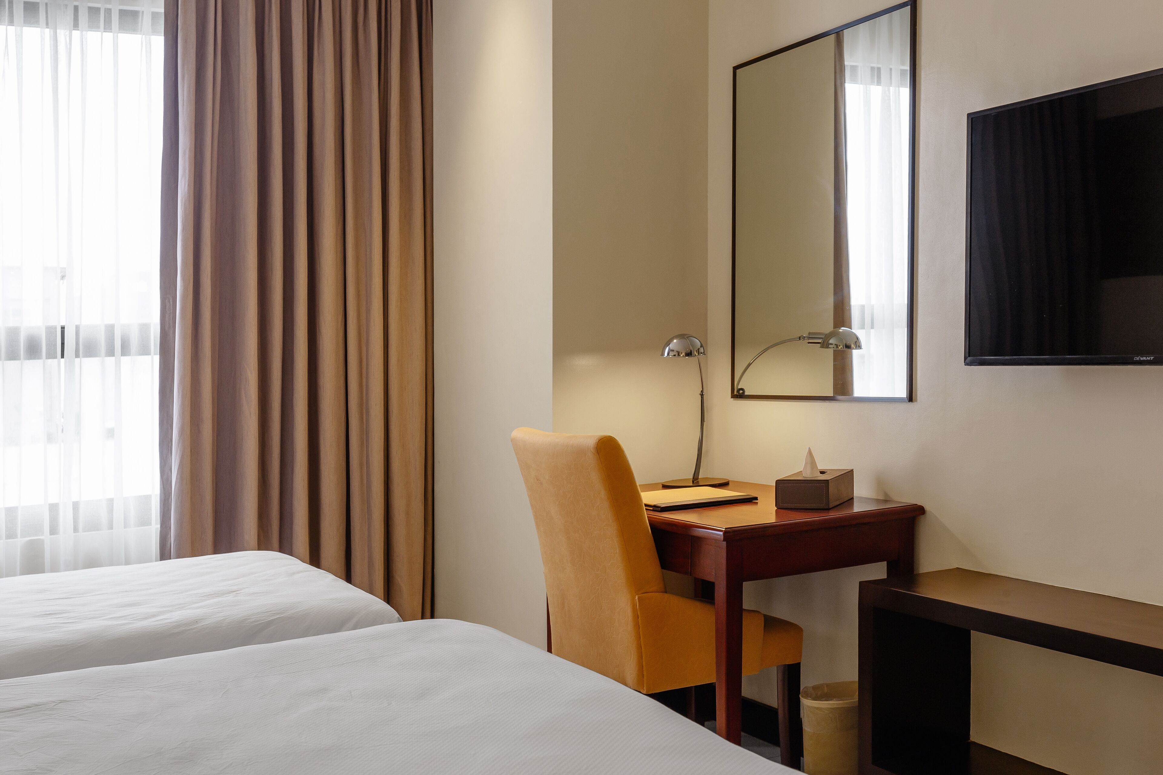 Habitación de hotel con dos camas, un escritorio con silla, una lámpara, un espejo y un televisor.