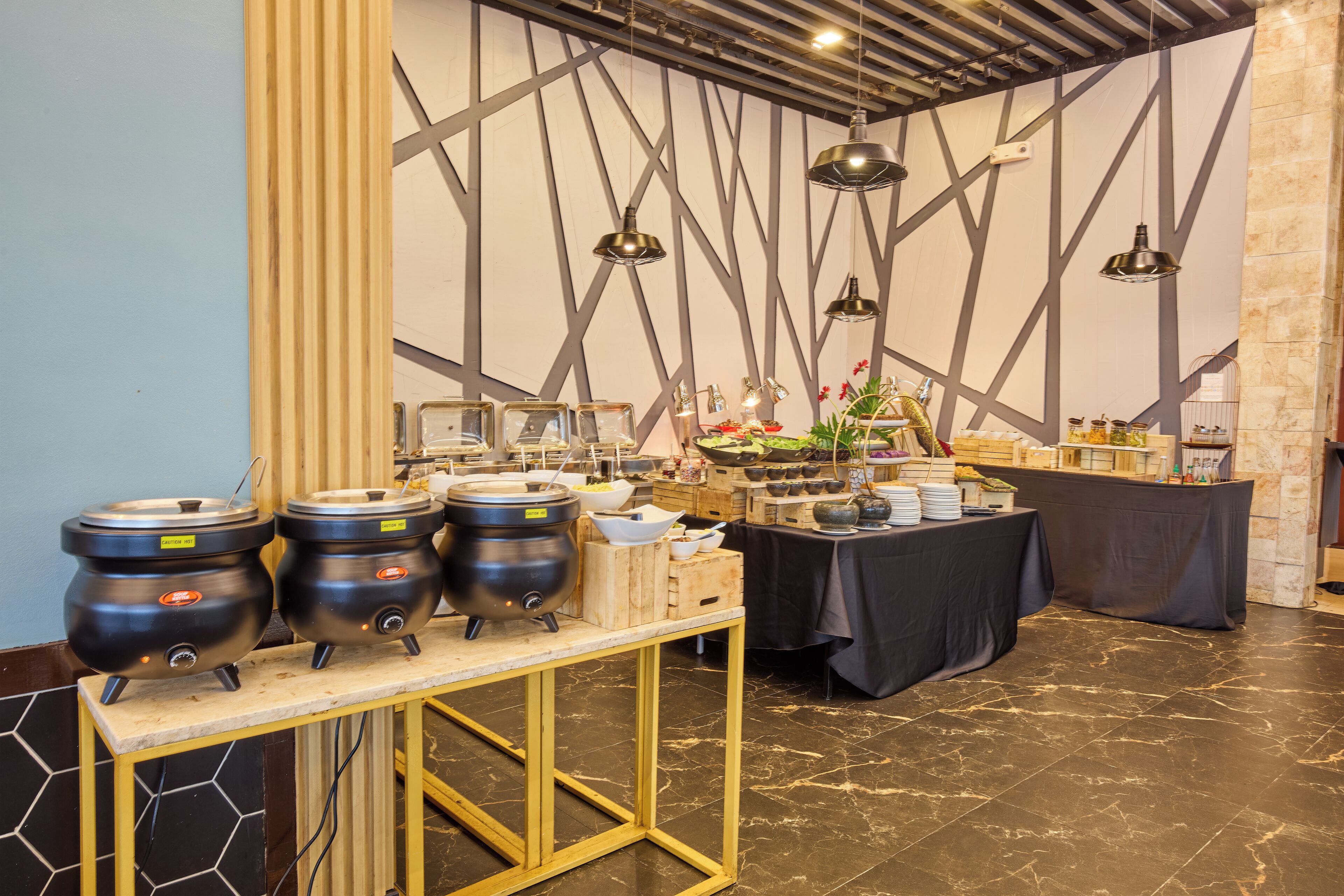 A buffet setup with multiple serving stations, including a central table with a black tablecloth and a wooden stand holding three large pots.