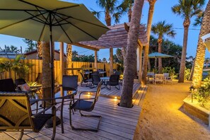 An outdoor patio area with wooden deck, outdoor seating, palm trees, and a pergola. - Modern, Cozy Efficiency Just Steps to the Beach! - Unit C (Cocoa Beach)