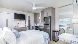A modern bedroom with a bed, a TV, a kitchenette, and a bathroom. - Modern, Cozy Efficiency Just Steps to the Beach! - Unit C (Cocoa Beach)