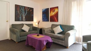 Uma sala de estar com dois sofás cinza, uma pequena mesa de centro e três quadros abstratos na parede.