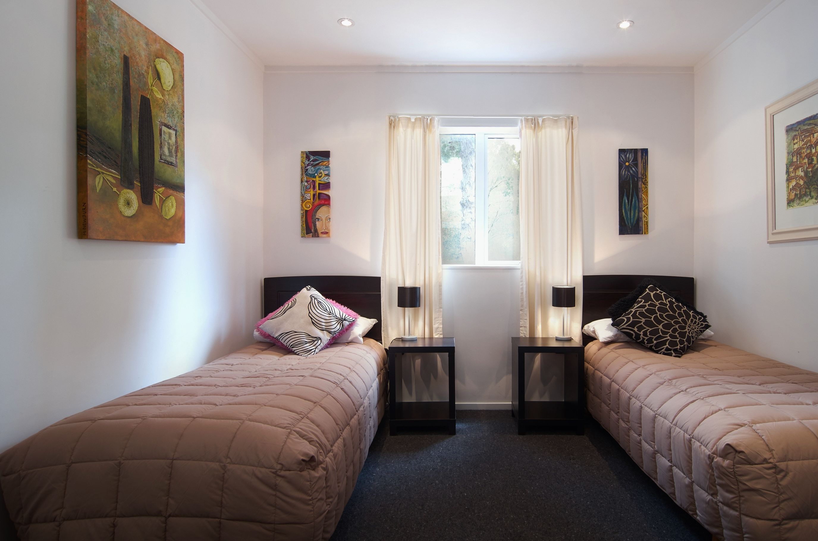 Una habitación de hotel con dos camas individuales, una ventana con cortinas y obras de arte en las paredes.