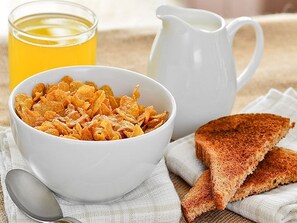 Kulhollinen muroja, paahtoleipää, lasi appelsiinimehua ja kannullinen maitoa pöydällä.