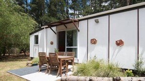 Uma casa móvel com um espaço de pátio, uma mesa e cadeiras, e uma barreira de troncos.