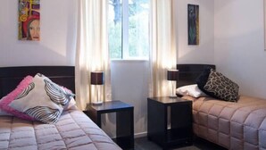Quarto com duas camas, uma janela com cortinas e obras de arte nas paredes.